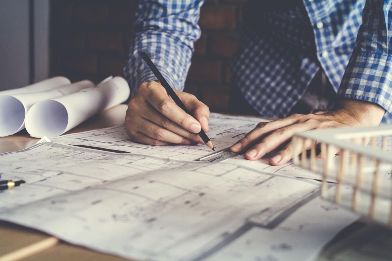 Mãos desenhando sobre plantas de arquitetura com lápis e régua